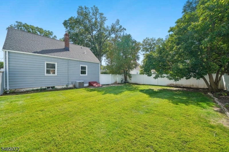 Backyard with a broad lawn, white privacy fence, mature trees, and blue-gray house.