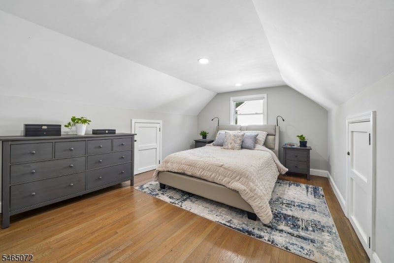 Attic bedroom with a centered bed, gray dressers, hardwood floors, and a patterned rug.