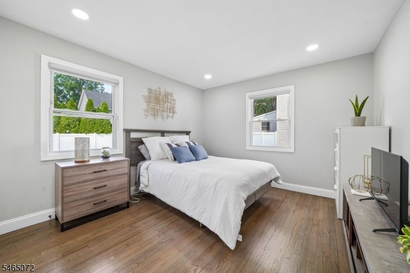 Bedroom with white and blue bedding, wood floors, two windows, and a matching dresser.