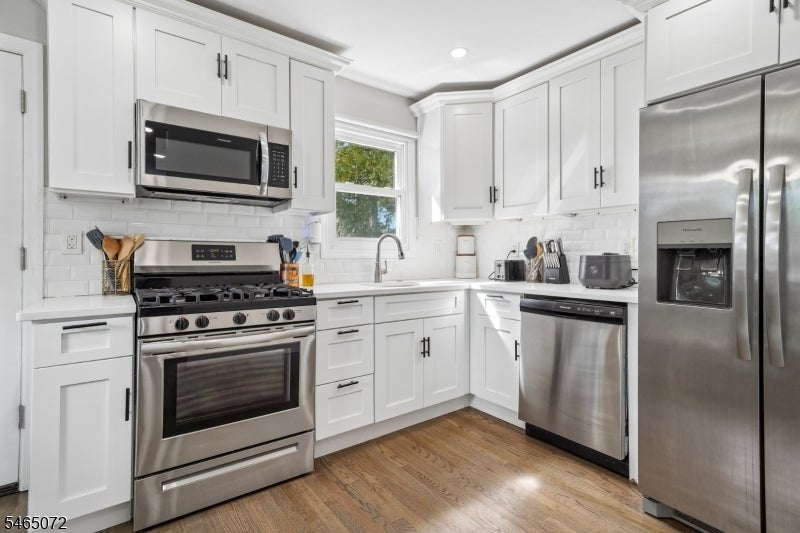 Kitchen with white shaker cabinets, stainless steel appliances, subway tile backsplash, and wood flooring.