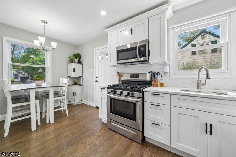 Bright white kitchen with stainless steel appliances, hardwood floors, and an adjoining dining area.