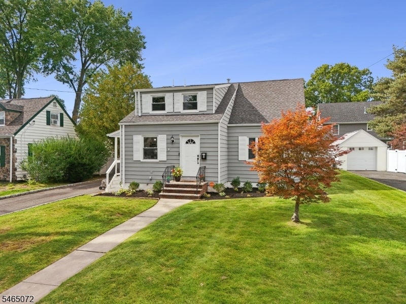 Gray two-story house with white trim, front steps, and an orange-leaved tree in the lawn.