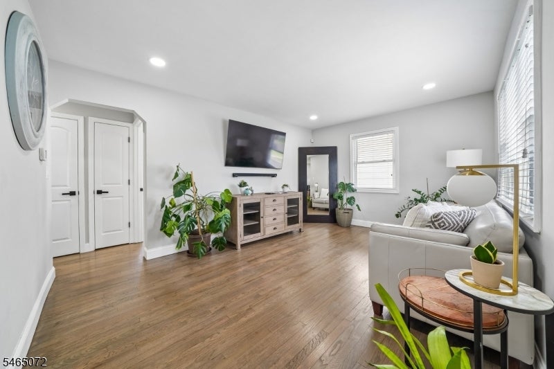 Furnished living room with wood floors, a white sofa, potted plants, and a wall-mounted television.