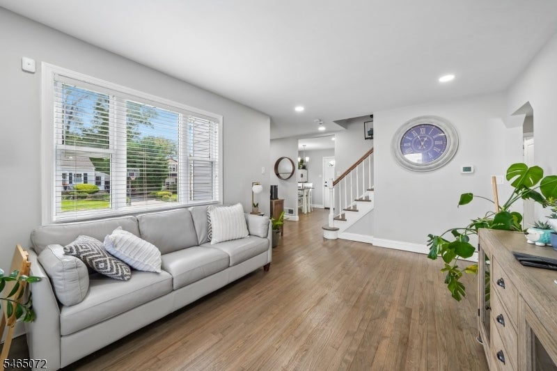 Living room with a gray sectional, large windows, wood flooring, and an open staircase.
