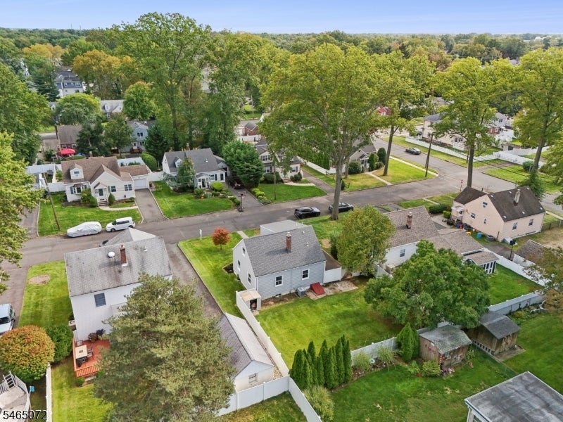 Aerial view of a gray two-story house with a fenced yard among leafy homes and tree-lined streets.