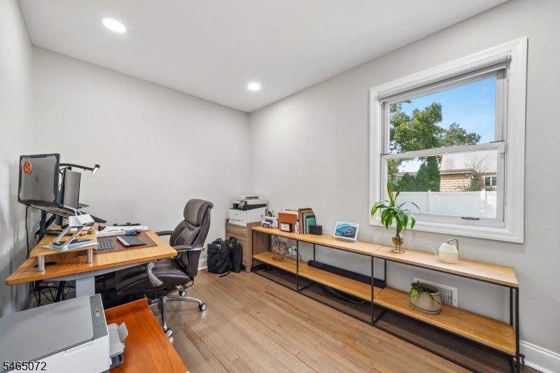 Home office with two workstations, wood floors, open shelving, and a large window.
