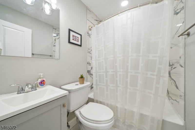 Bathroom with a white vanity, toilet, and bathtub behind a geometric-patterned shower curtain.
