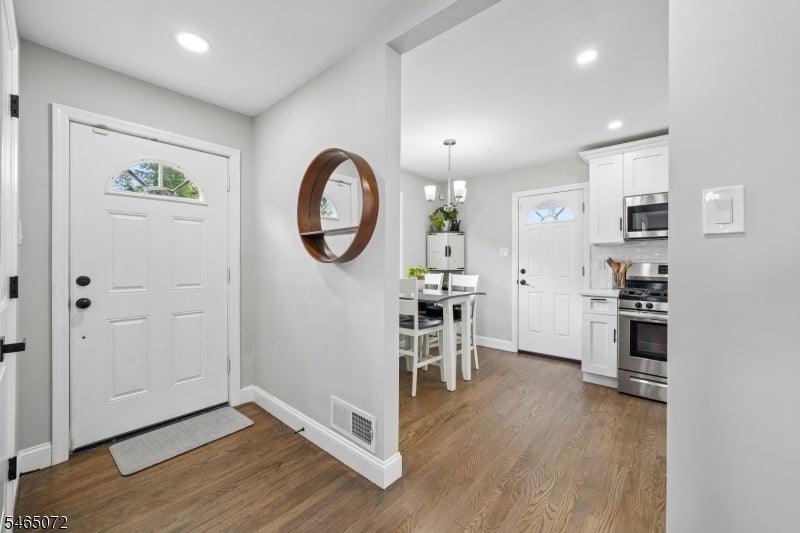 Entryway with a white front door, wood-look flooring, and an open view into the kitchen and dining area.