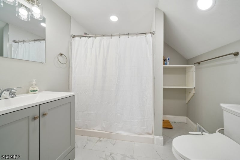 Bathroom with a white shower curtain, gray vanity, and marble-look tile floor.