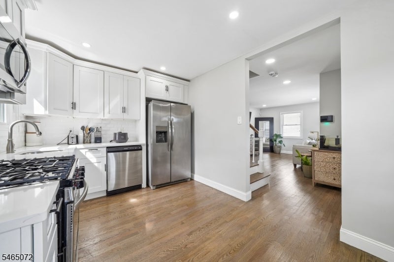 Kitchen with white cabinets, stainless steel appliances, hardwood floors, and an opening to the living area.