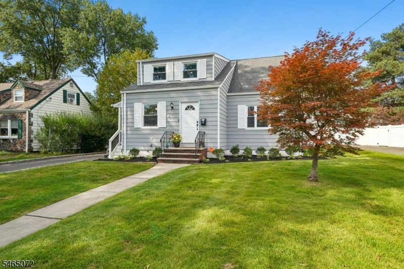 Gray-sided house with a front dormer, small porch, and red-leaved tree in the lawn.