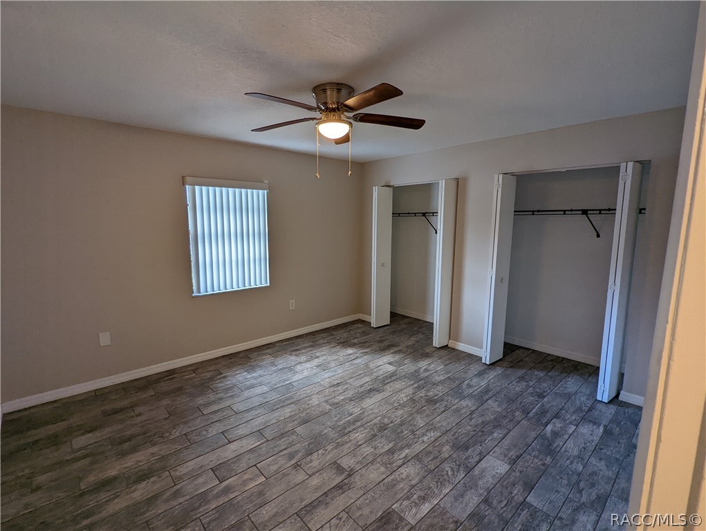 Empty bedroom with two open closets, wood-look plank flooring, and a ceiling fan.