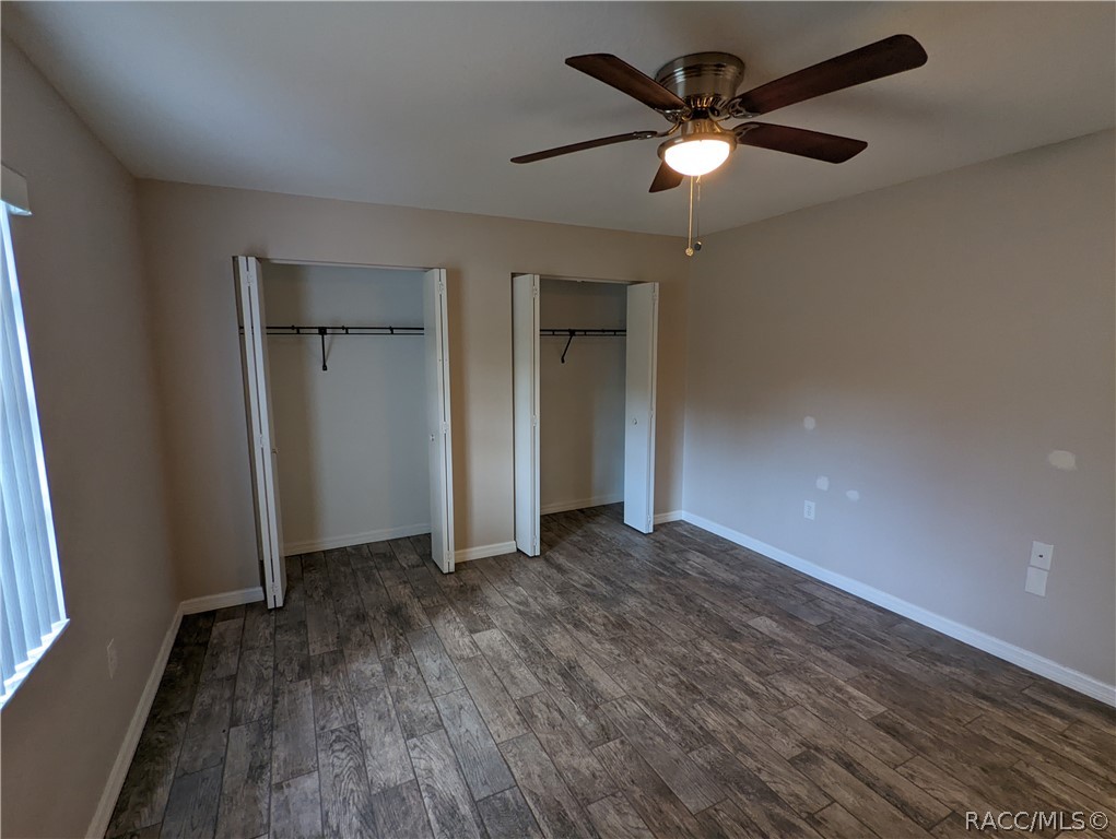 Vacant bedroom with two open closets, plank flooring, and a ceiling fan.
