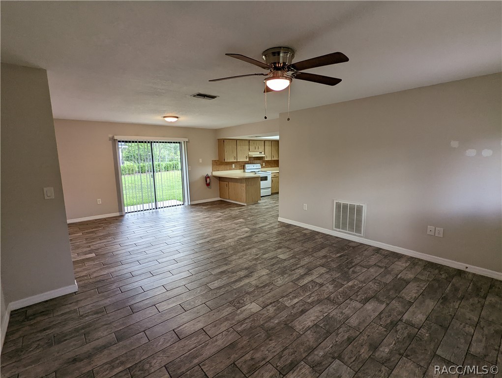 Vacant living area with wood-look tile, ceiling fan, sliding doors, and an adjoining kitchen.