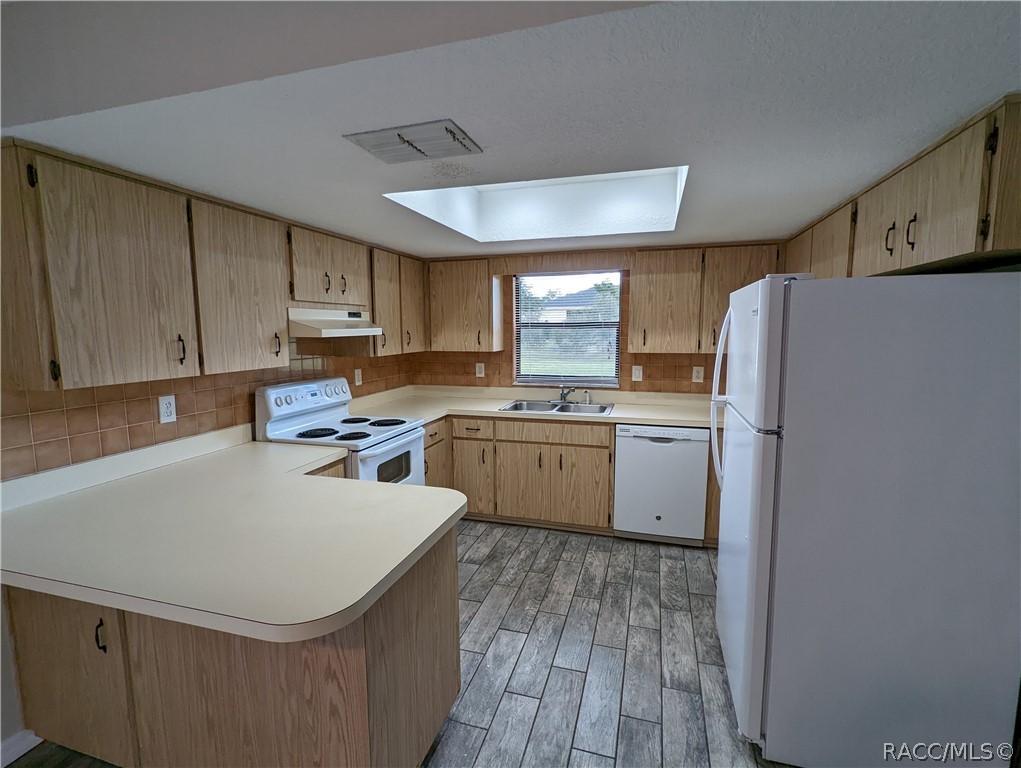Kitchen with wood cabinets, a white peninsula, and a skylight above the tiled floor.