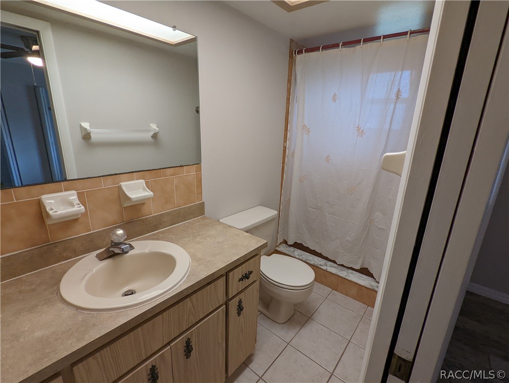 Bathroom with a woodgrain vanity, large mirror, toilet, and shower behind a white curtain.