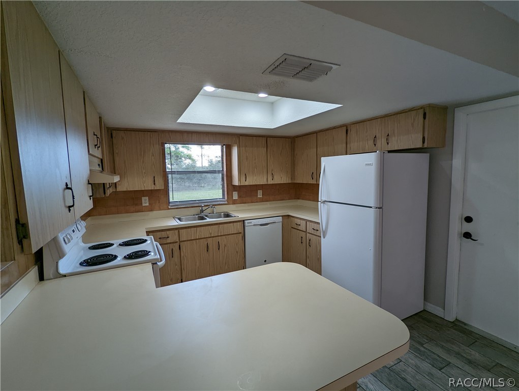Kitchen with oak cabinets, white appliances, a peninsula counter, and a skylight.