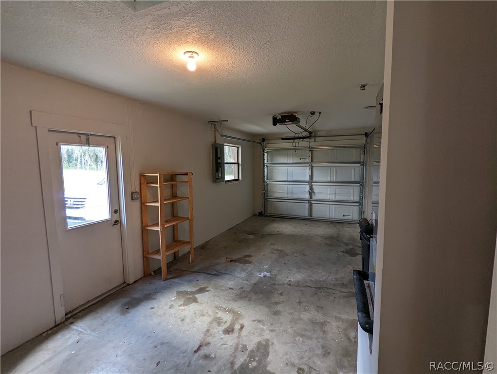 Empty garage with a concrete floor, closed sectional door, and wooden shelving.
