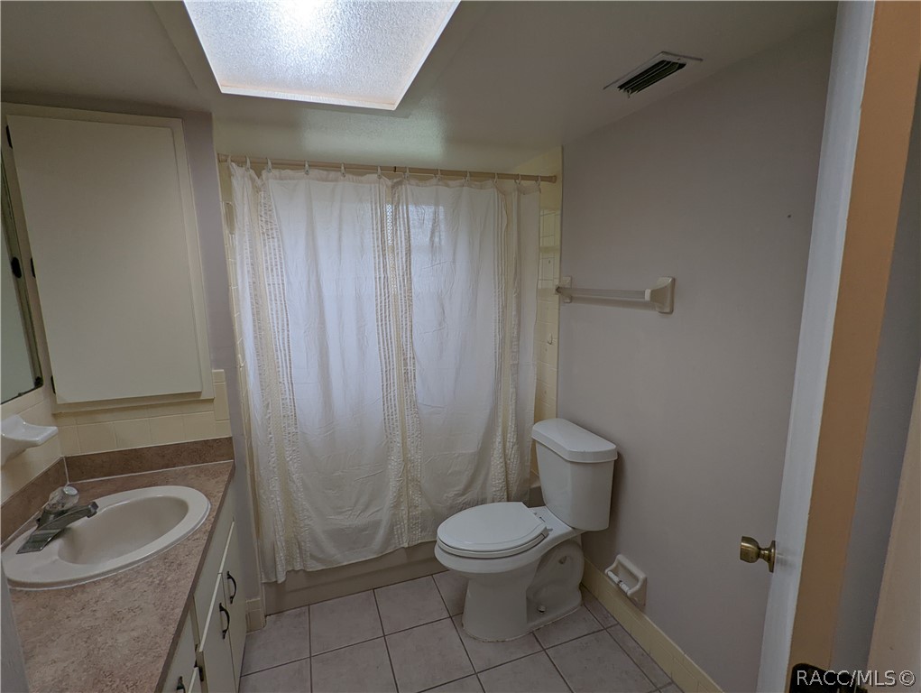 Bathroom with a curtained tub and shower, toilet, and single-sink vanity.