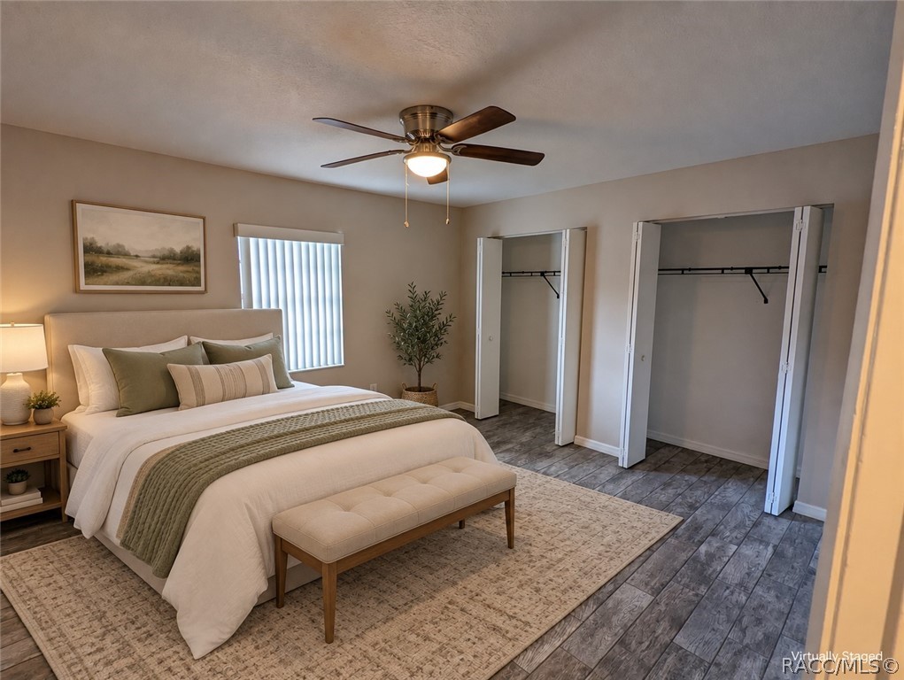 Virtually staged bedroom with a white bed, green pillows, upholstered bench, and two open closets.