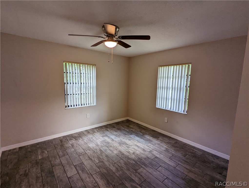 Vacant room with wood-look tile flooring, two windows with vertical blinds, and a ceiling fan.