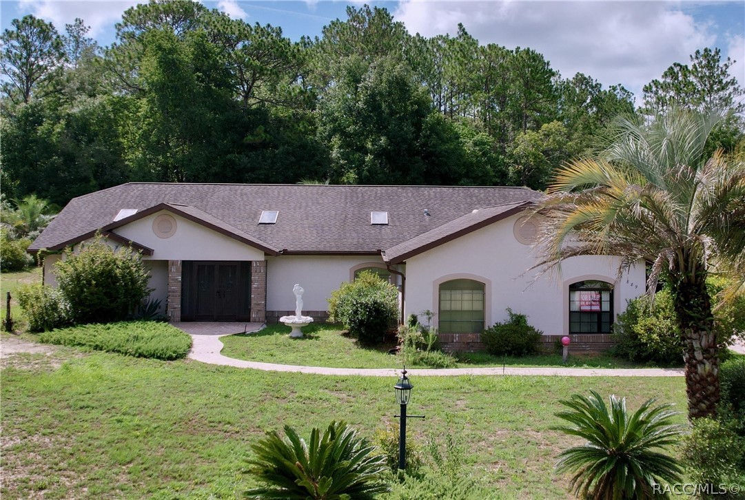 Single-story stucco home with arched windows, a curved walkway, and palms in the front yard.