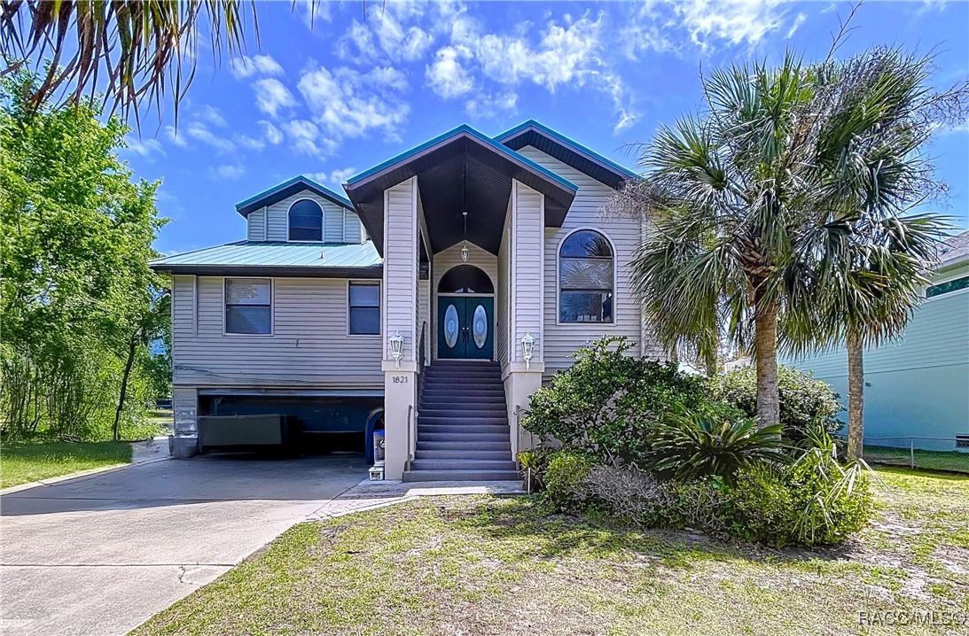 Raised house with a tall central staircase, metal roof, and palm trees.