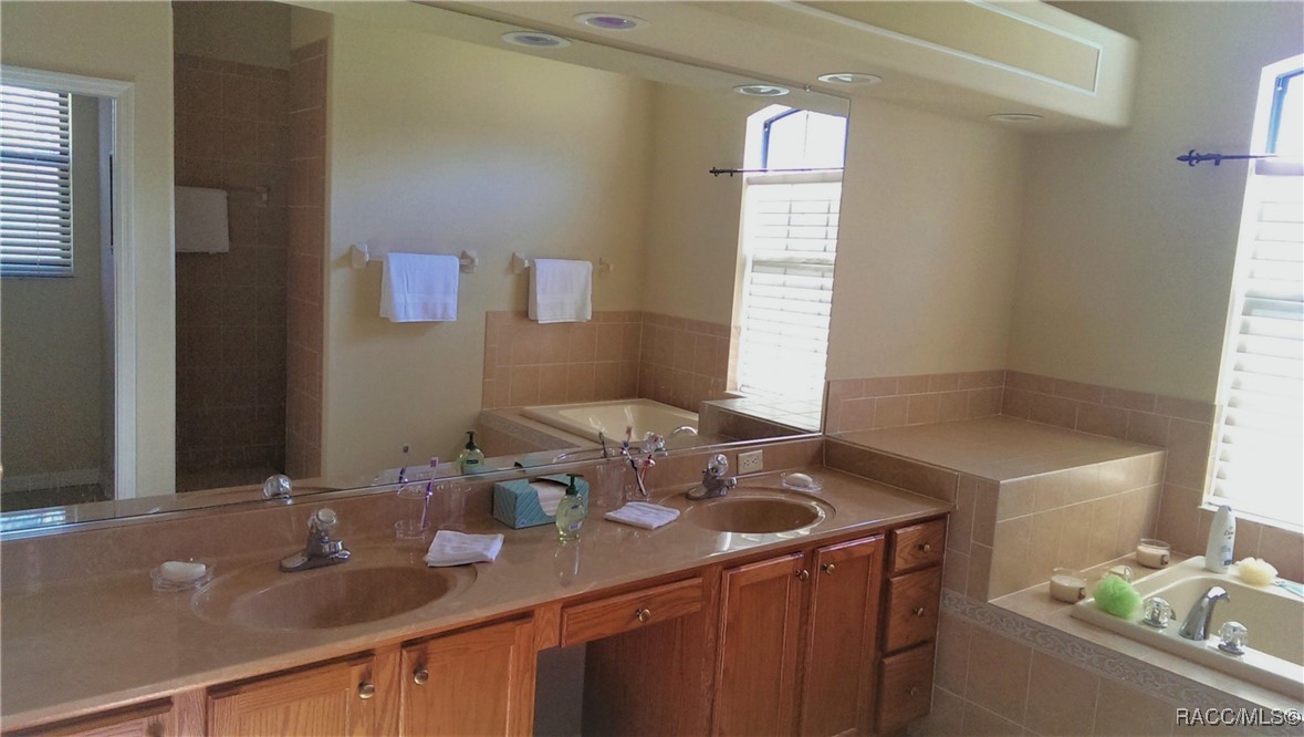 Bathroom with a double-sink vanity, wood cabinets, and a tiled soaking tub.