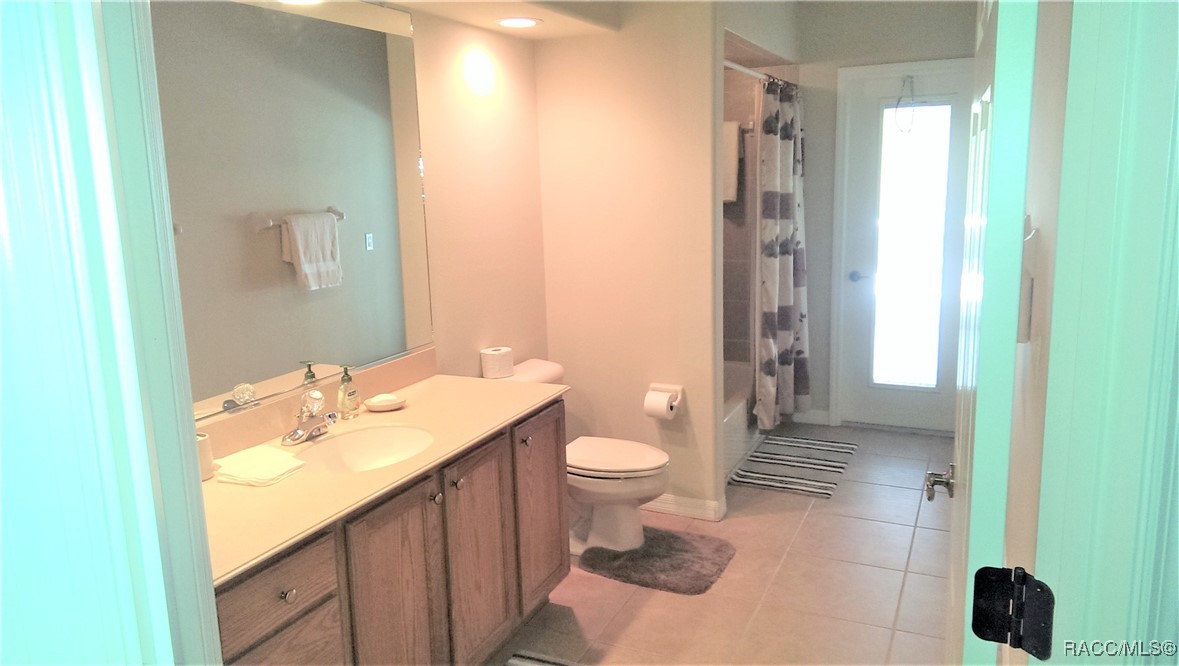 Bathroom with a long wood vanity, tiled floor, toilet, and curtained shower.