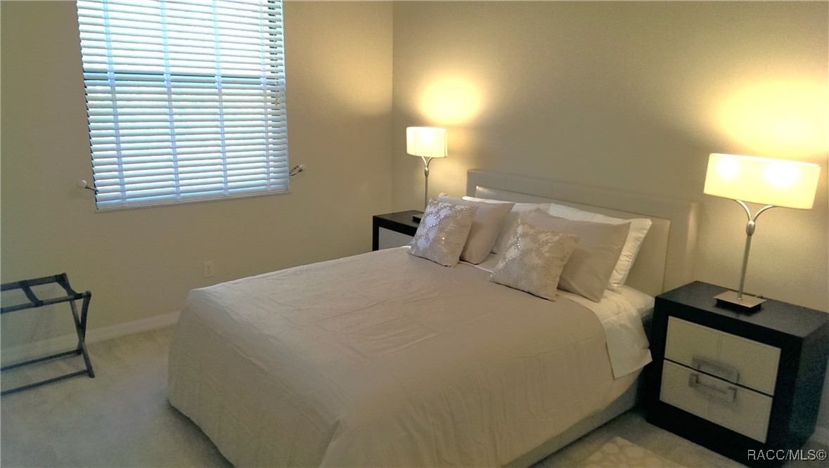 Furnished bedroom with a large white bed, matching bedside lamps, and a window with blinds.