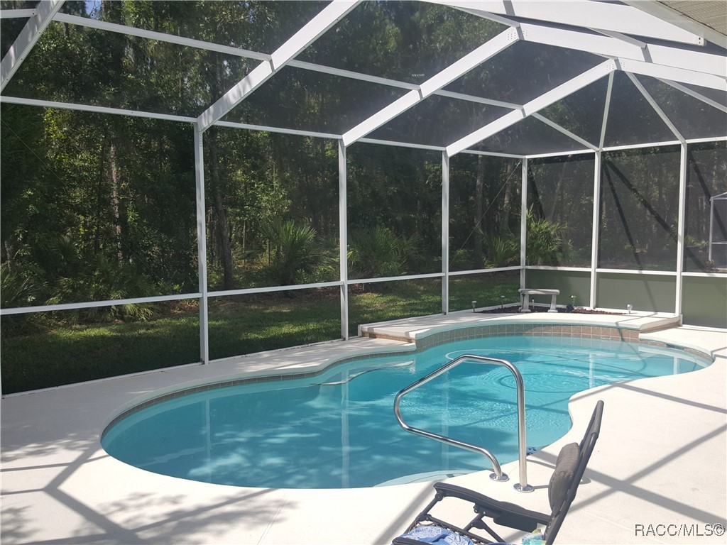 Curved swimming pool in a screened enclosure, with lounge chairs and trees visible beyond.