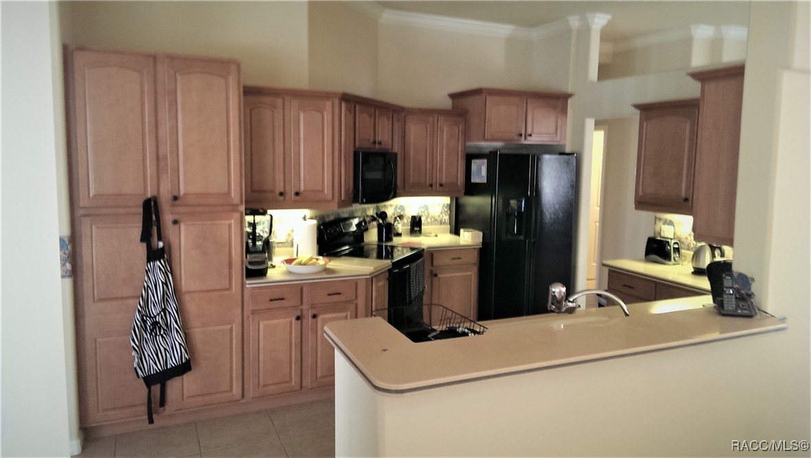 Kitchen with reddish wood cabinets, black appliances, and a long peninsula with a sink.