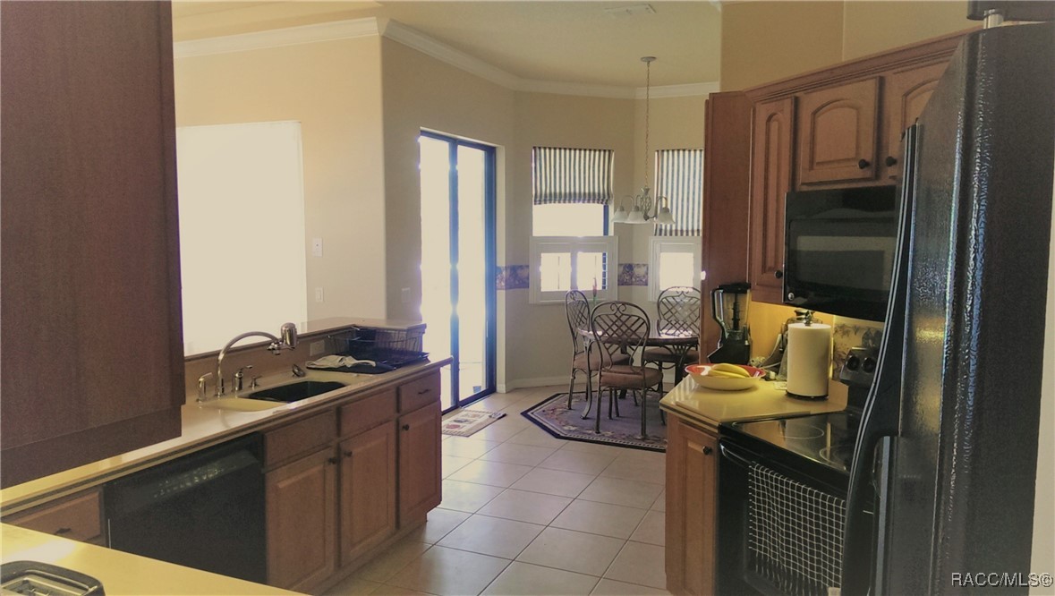 Kitchen with wood cabinetry, dark appliances, tiled floors, and a dining nook by bright windows.