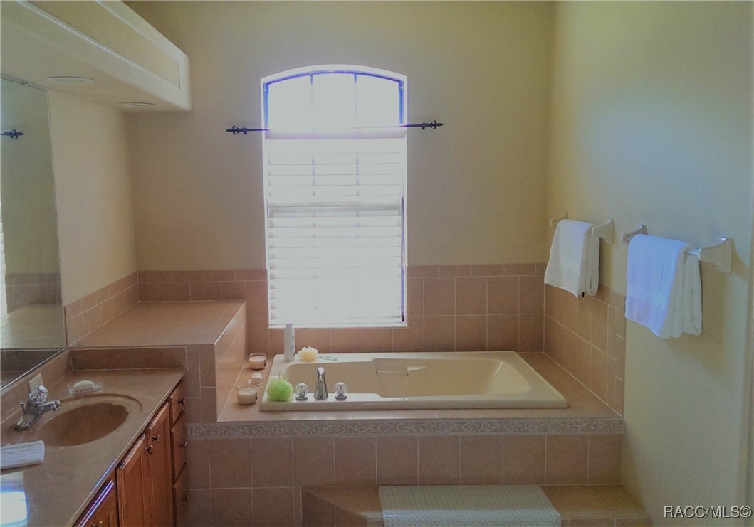 Bathroom with a built-in soaking tub beneath an arched shuttered window and a wood vanity.