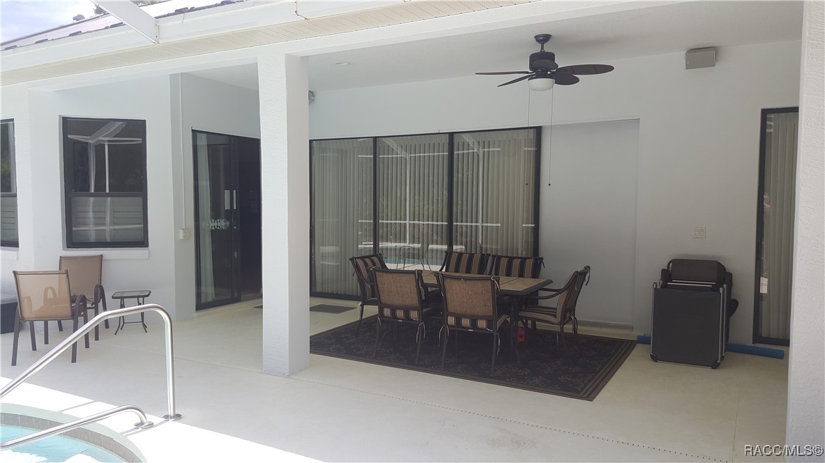 Covered patio with outdoor dining set, ceiling fan, and pool edge.
