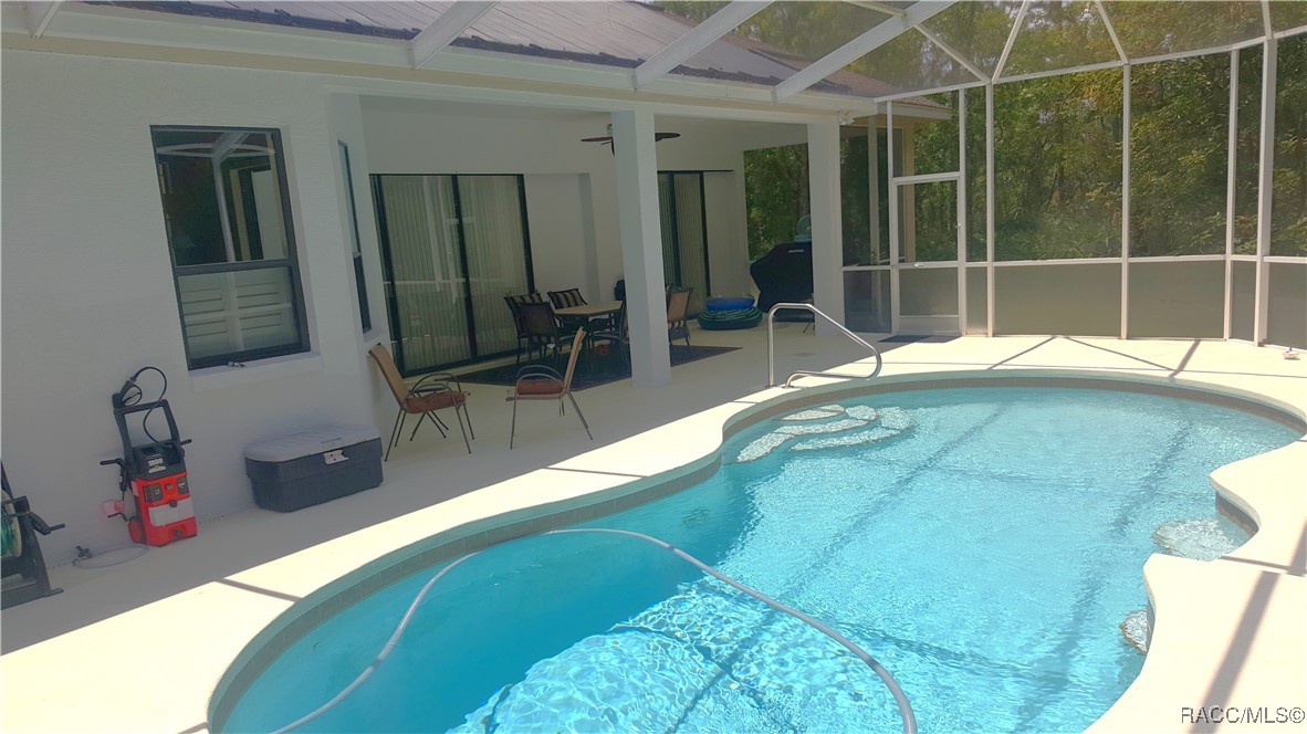 Swimming pool in a screened enclosure beside a covered patio with outdoor dining furniture.