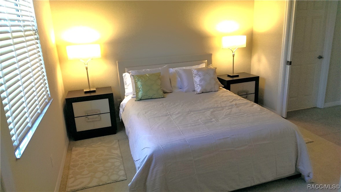 Bedroom with a large white bed, matching bedside tables, warm lamps, and a window with white blinds.