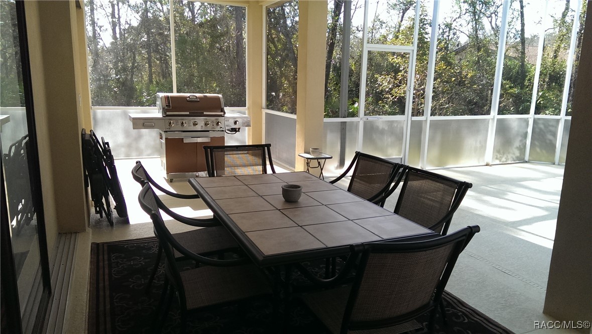 Screened patio with a tiled dining table, outdoor grill, and wooded views.