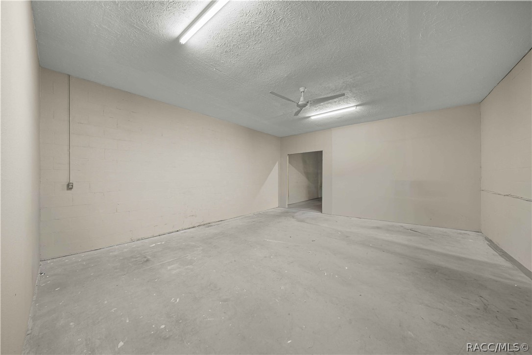 Vacant unfinished room with a concrete floor, painted block walls, ceiling fan, and fluorescent lights.