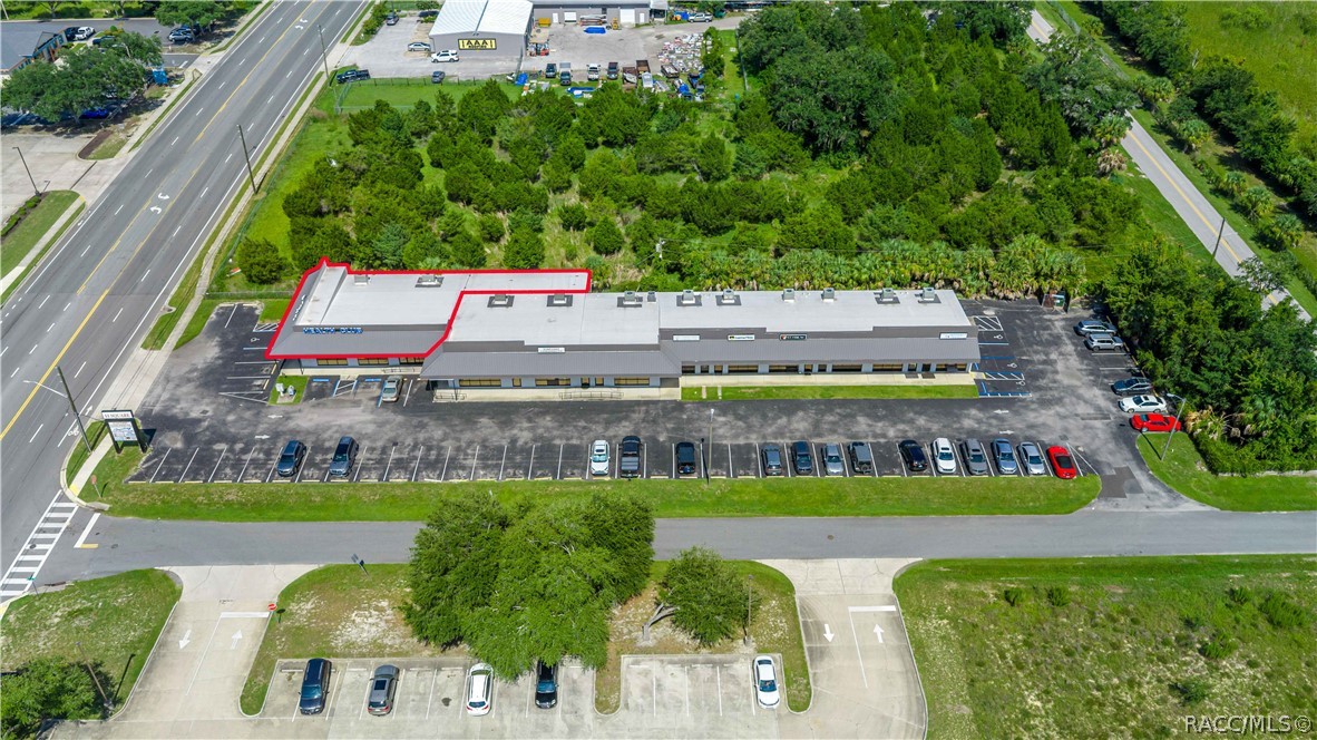 Aerial view of a single-story commercial building with a large parking lot and part of its roof outlined in red.