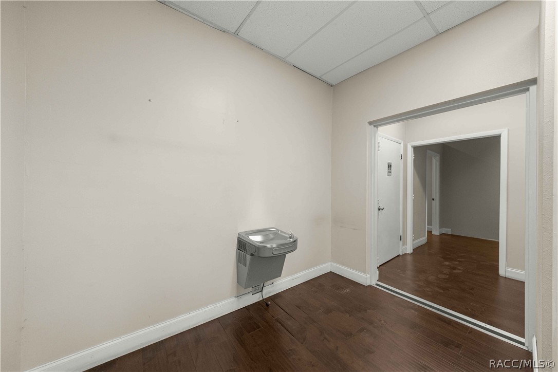 Empty room with dark wood flooring, a wall-mounted drinking fountain, and an open doorway.