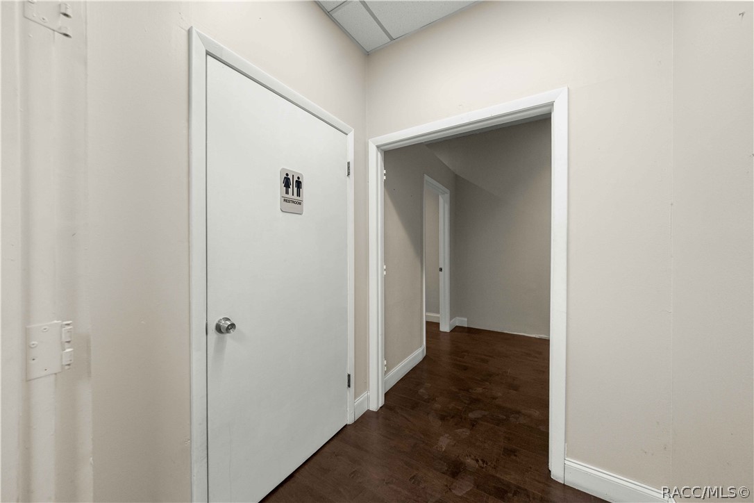 Hallway with dark wood flooring, a restroom door, and an open doorway.