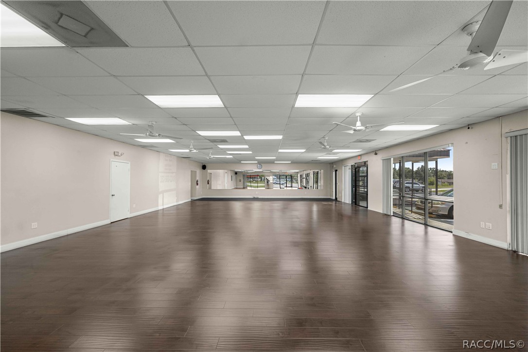 Empty commercial interior with dark wood-look flooring, ceiling fans, and glass storefront windows.