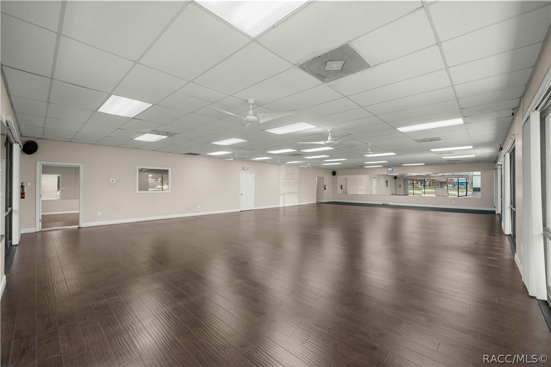 Vacant commercial space with dark wood-look flooring, ceiling fans, and windows along two walls.