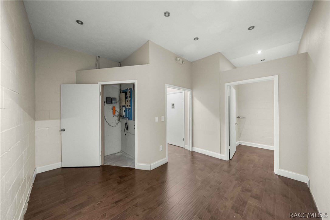 Empty room with dark wood-look flooring, recessed lights, and an open electrical panel closet.