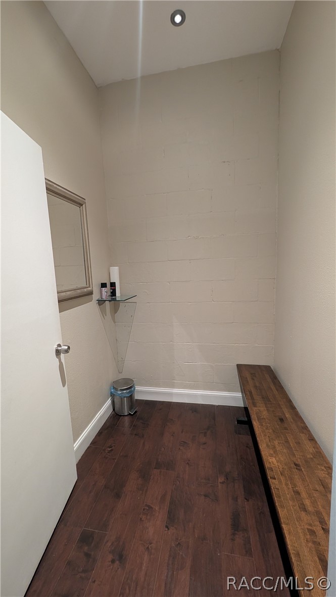 Narrow interior room with dark wood flooring, a long wooden bench, and a wall-mounted mirror.