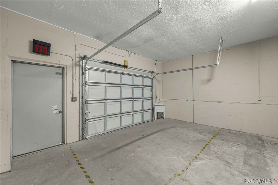 Empty garage with a sectional overhead door, gray exit door, and concrete floor.