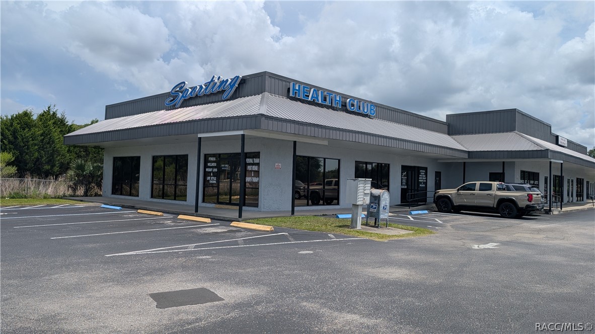 Commercial health club building with prominent rooftop signage and a paved parking lot.