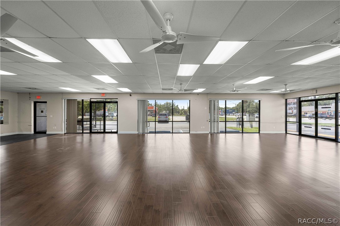 Vacant commercial storefront with dark wood-look flooring and a wall of windows and glass doors.
