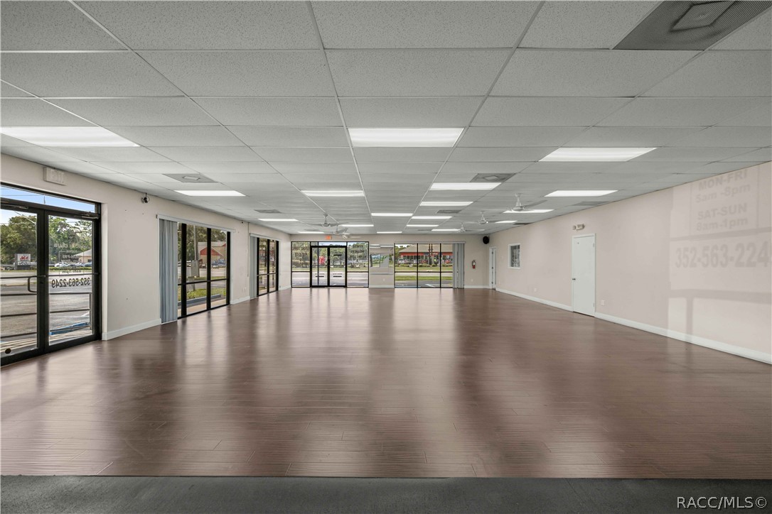 Vacant commercial storefront with a broad wood-look floor and large street-facing windows.